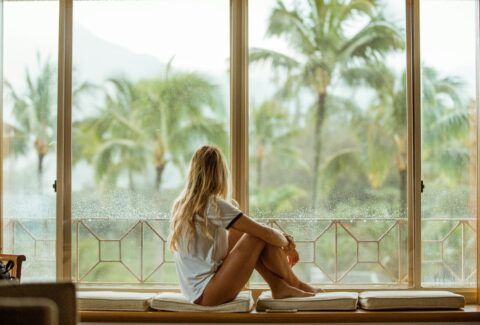 woman sitting on white cushion near glass window